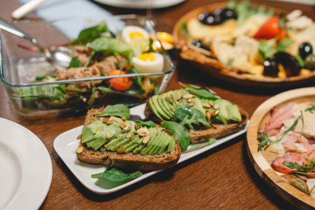 pan de molde integral junto a acompañamientos sanos, como el aguacate, semillas y rúcula y otros alimentos saludables como el huevo lechuga y tomate