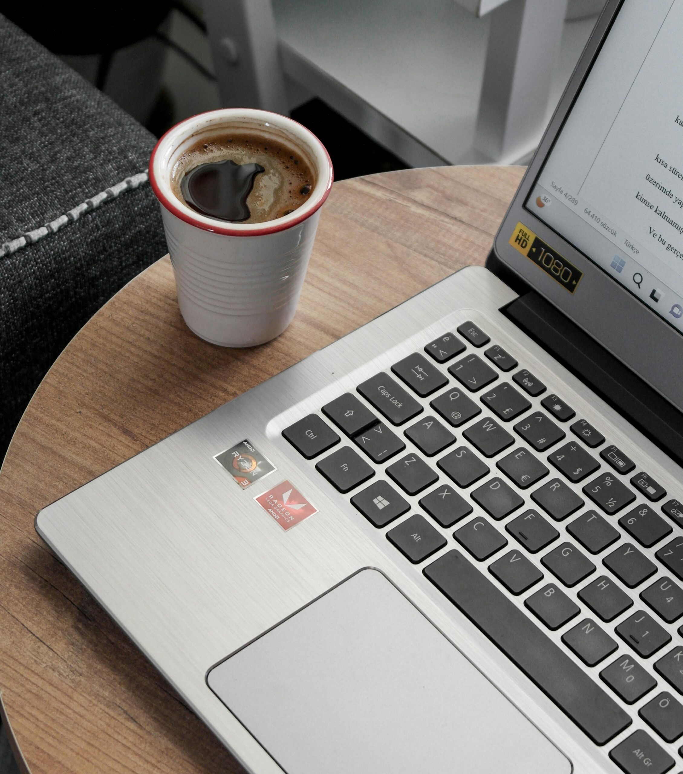 Imagen de un computador con un café en una taza blanca con borde rojo.