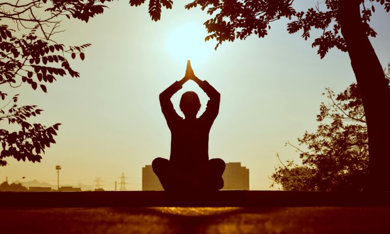 mujer haciendo una posición de yoga frente al atardecer