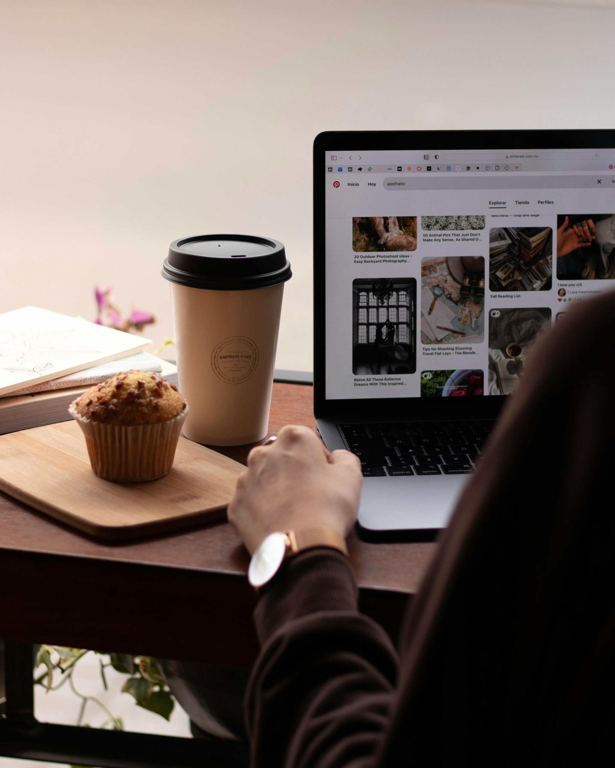 Un hombre trabajando en una laptop en una cafetería, con una taza de café y un muffin frente a él