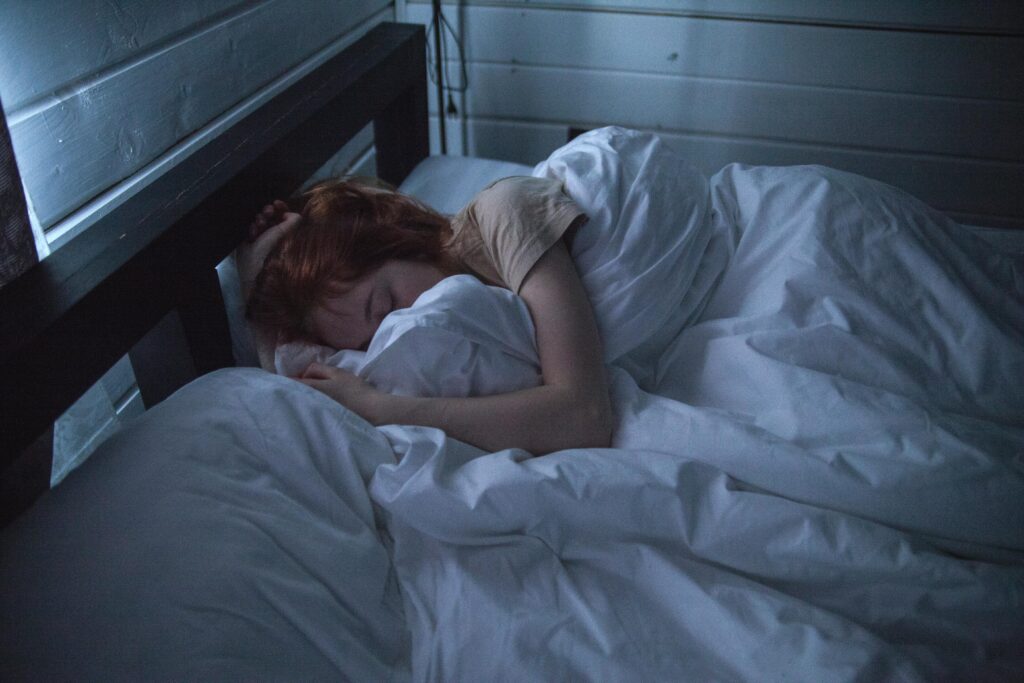 mujer joven durmiendo en su cama de color blanco en su habitación a oscuras